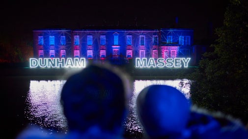 A couple gaze at the house illuminated in festive lights at Christmas at Dunham Massey, Cheshire.